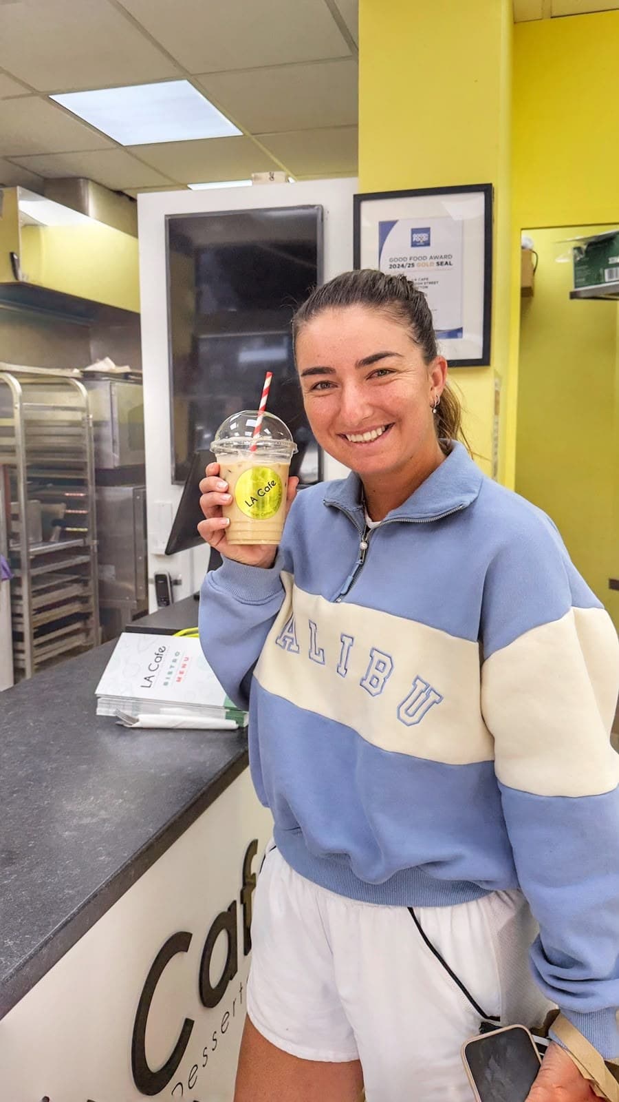 Jessica Failla smiling with an LA Cafe iced coffee at the counter